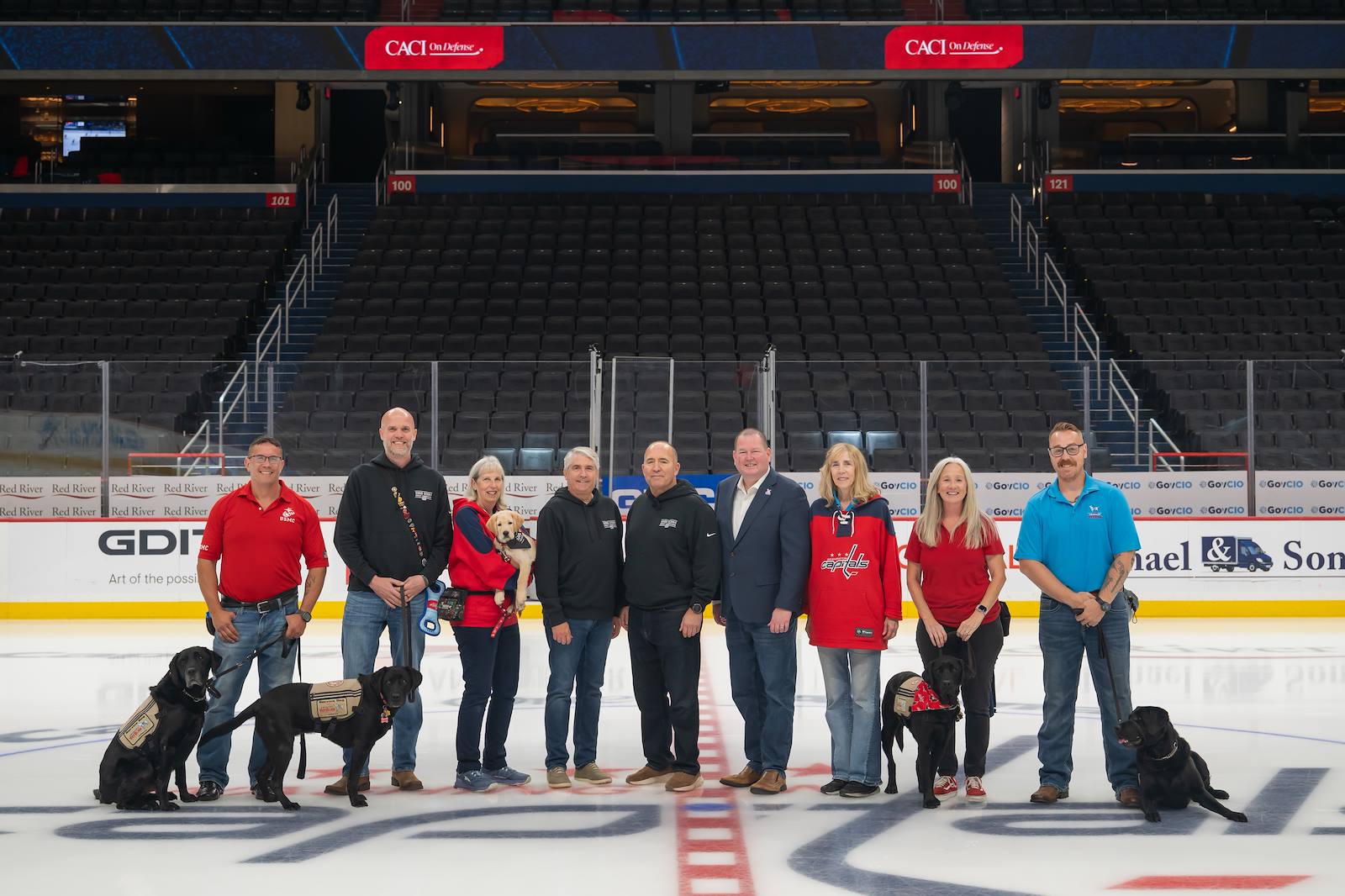 From left: Veteran Chris Sunday and Eddie, veteran and CACI employee Harley Brown with Claire, trainer Millie Jernigan holding CACI's first Good Dog - Bravo, President and CEO John Mengucci, CACI's Good Dogs Ambassador Mike Shields, America's VetDogs CEO John Miller, trainer Melissa Harrington, veteran Deana Stone with Gunner, and veteran Paul Sullivan with Sal.